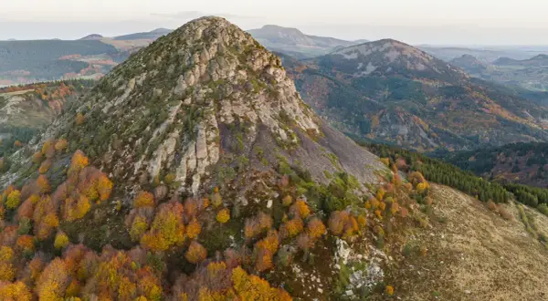 Vue aérienne du Mont Gerbier de Jonc en automne, ses pentes rocheuses et ses forêts aux couleurs flamboyantes. Une carte visuelle de ce paysage volcanique.
