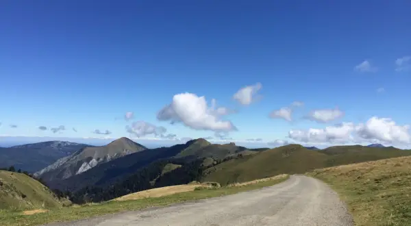 Route sinueuse menant au port de Bales, traversant des paysages de montagnes verdoyantes sous un ciel bleu éclatant.