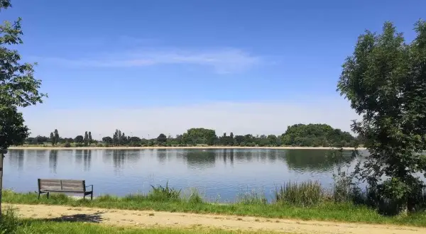 Un banc invite à la contemplation du lac de la Ramée sous un ciel bleu.