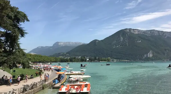 Vue animée de la plage de l'Impérial avec des pédalos et des montagnes en arrière-plan.