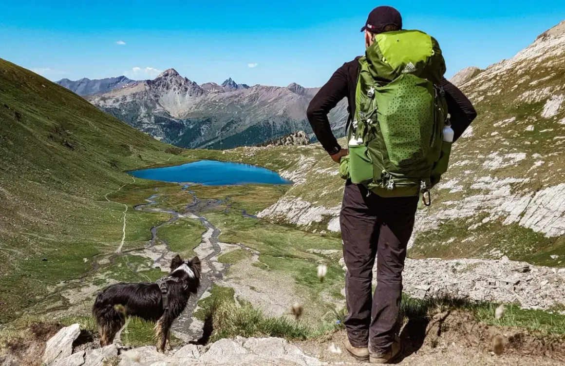 Un randonneur et son chien contemplent un lac bleu et des montagnes majestueuses. Une belle randonnée avec chien.