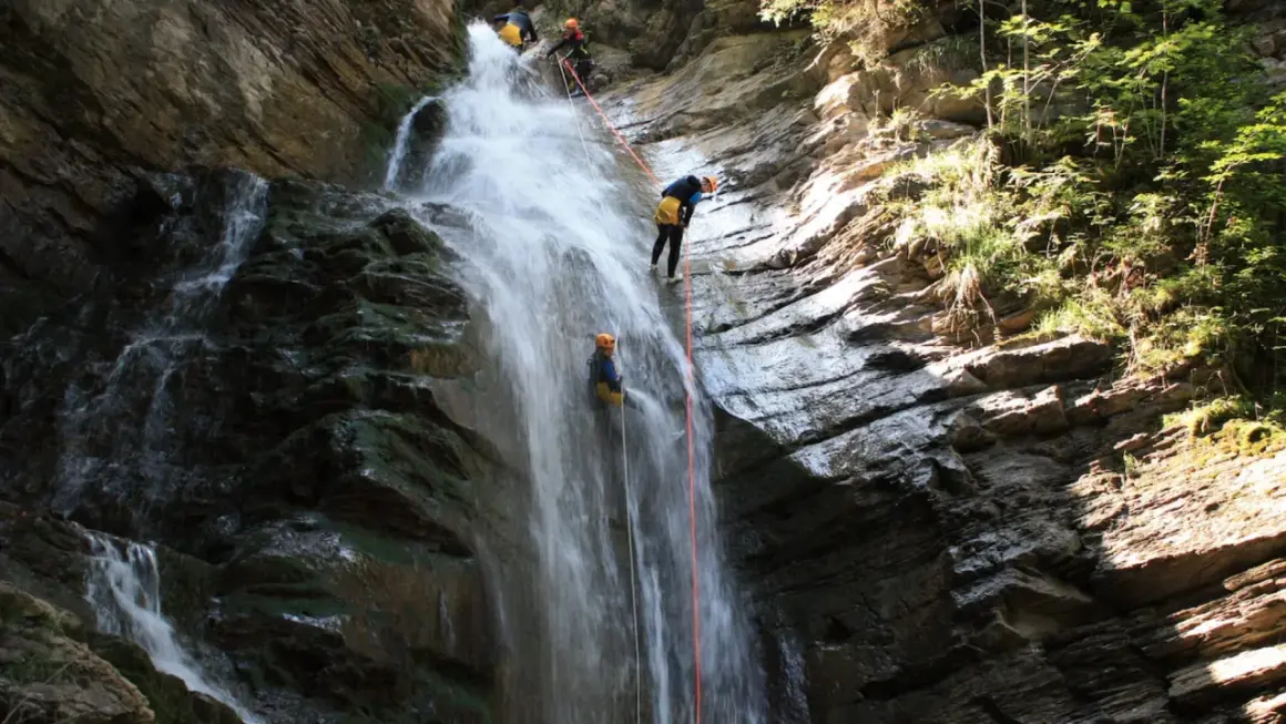 Descente en rappel le long de la cascade de Nyon. Des canyoneurs descendent une chute d'eau spectaculaire, entourés par la roche et la végétation luxuriante.
