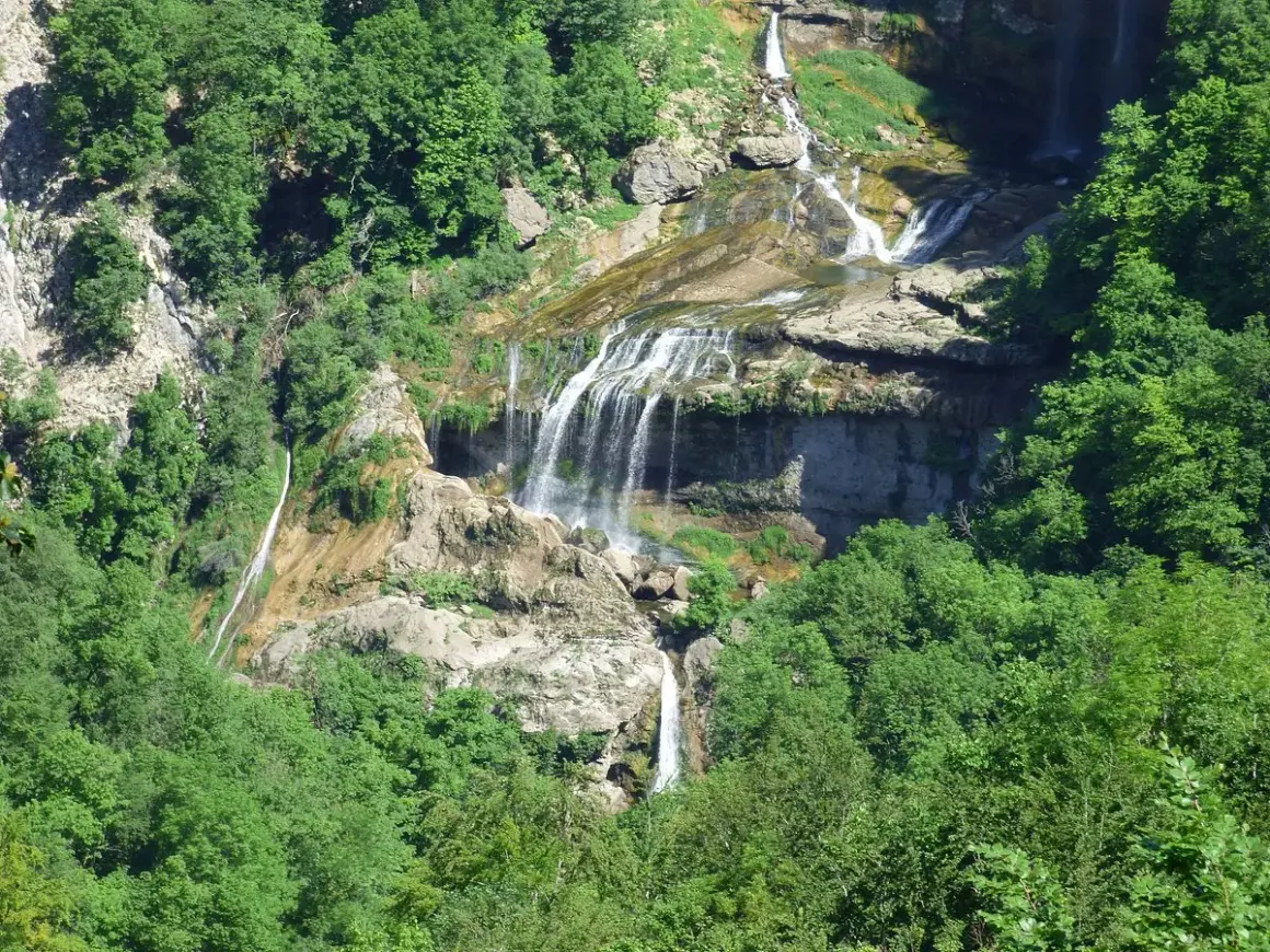La cascade de la Charabotte dévale une falaise rocheuse, entourée d'une végétation luxuriante. L'eau forme de multiples bras sur les rochers.