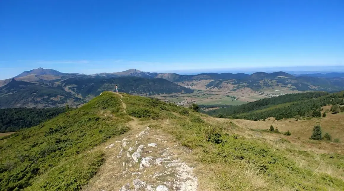 Vue panoramique depuis le col du Chioula, avec un randonneur contemplant les montagnes verdoyantes et le ciel bleu.