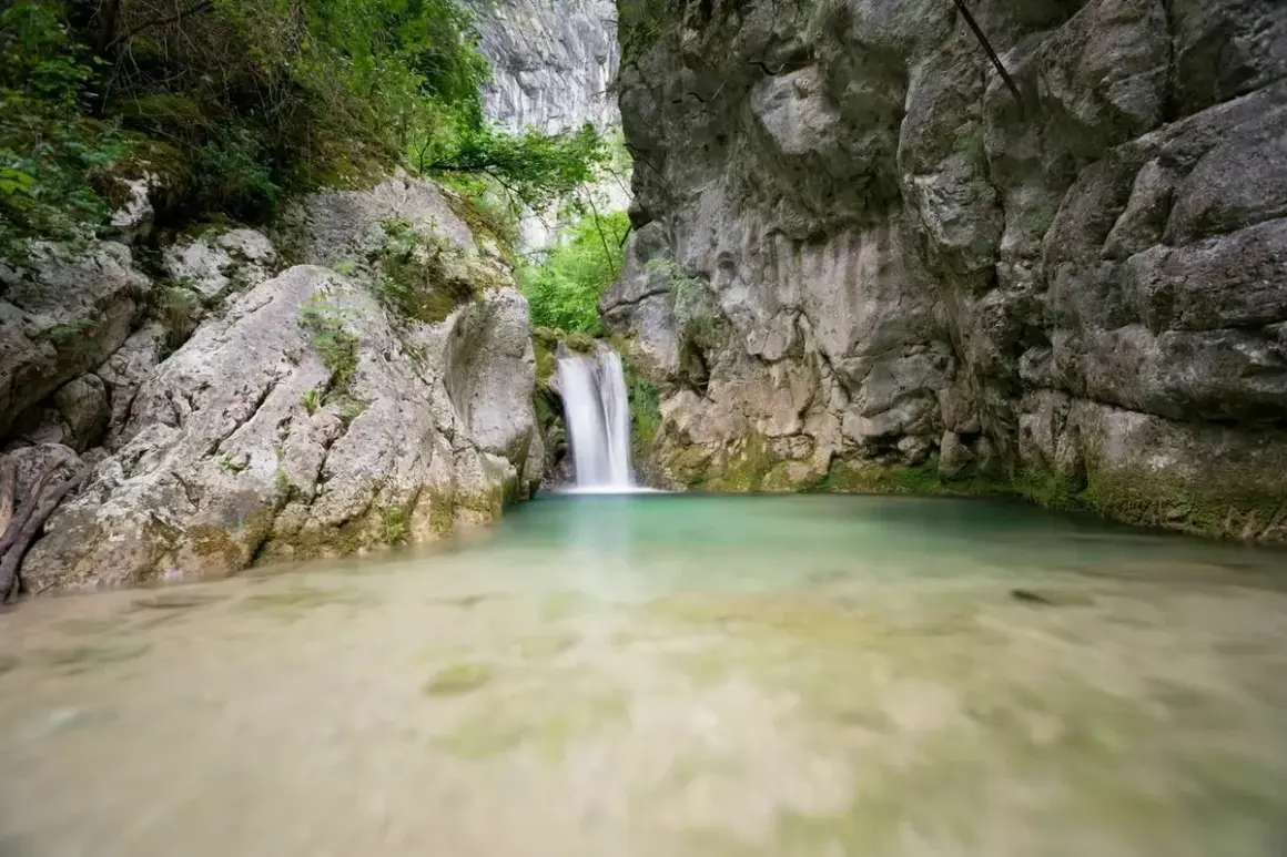 Cascade d'eau tombant dans un bassin turquoise au cœur de la gorge du Nan, entourée de falaises rocheuses et de végétation luxuriante.