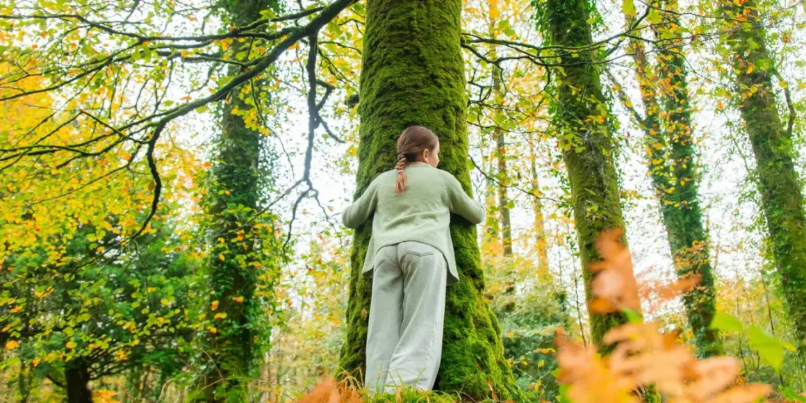 Une jeune fille enlace un arbre couvert de mousse dans une forêt aux couleurs d'automne. La **forêt de rennes** est un lieu magique.