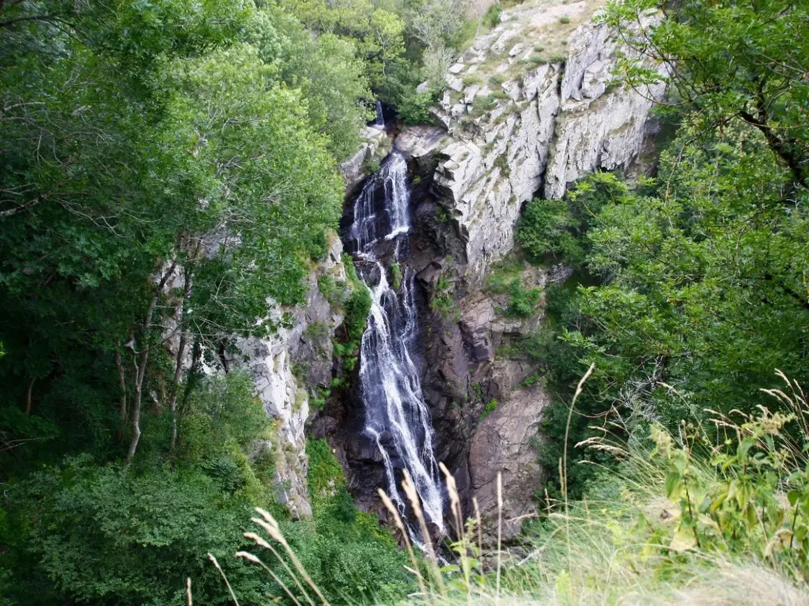 La cascade de Cubserviès dévale une falaise rocheuse, entourée d'une végétation luxuriante. L'eau blanche contraste avec le sombre des rochers.