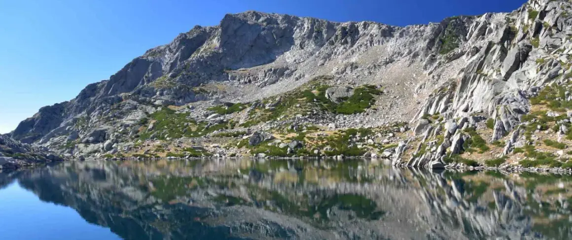 Reflets parfaits des montagnes rocheuses sur le lac de Bastani, sous un ciel bleu éclatant.