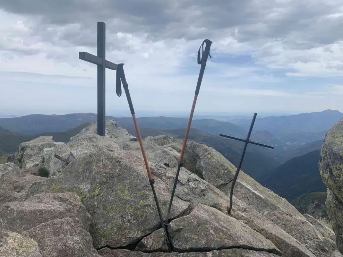 Sommet du pic des 3 Seigneurs. Deux croix et des bâtons de randonnée sur un rocher, avec une vue panoramique sur les montagnes.