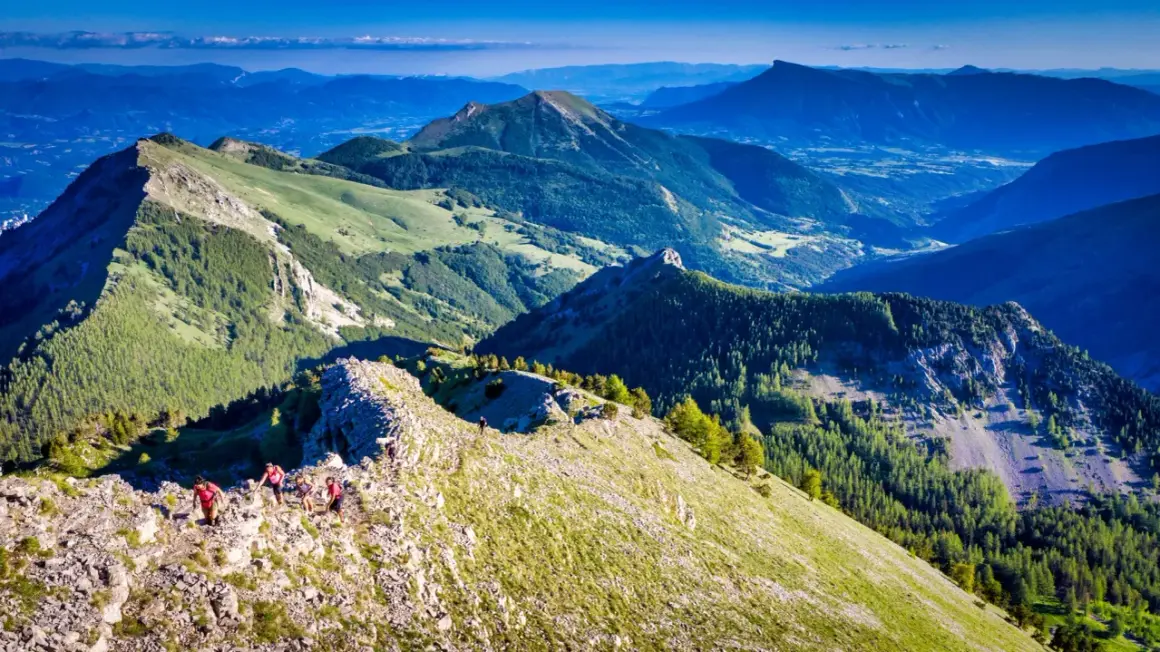 Randonneurs sur la crête rocheuse menant au pic de Gleize, avec des montagnes verdoyantes et un ciel bleu.