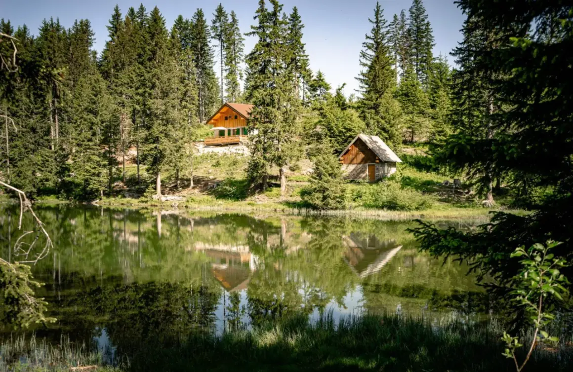 Reflets parfaits des chalets et des sapins dans le lac du Poursollet, un paysage de montagne paisible.