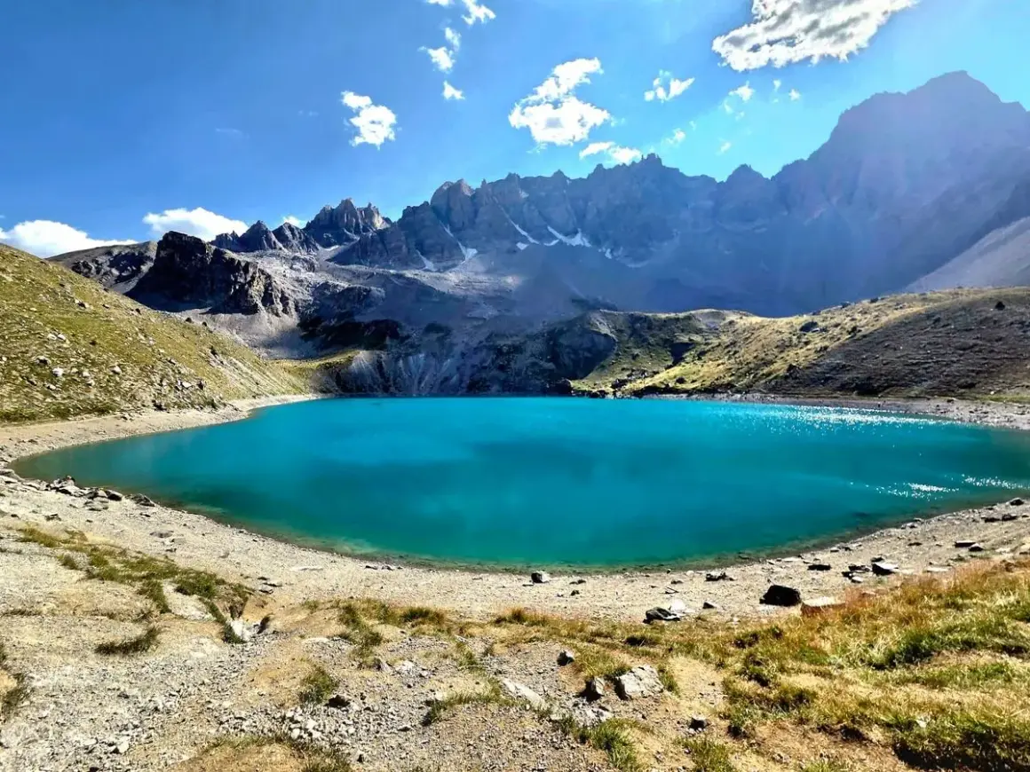 Magnifique lac Saint-Anne aux eaux turquoise, entouré de montagnes rocheuses et de pentes herbeuses sous un ciel bleu éclatant.