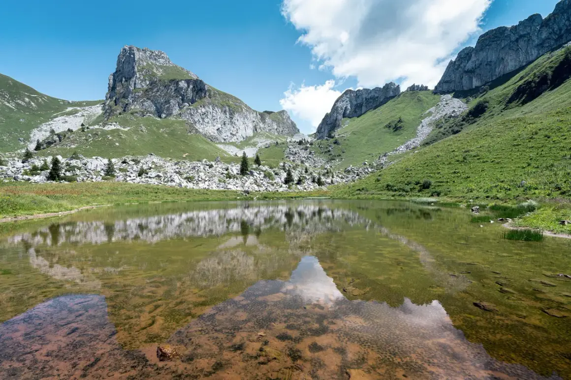 Le lac de Darbon, paisible, reflète les montagnes verdoyantes et rocheuses sous un ciel bleu et nuageux.