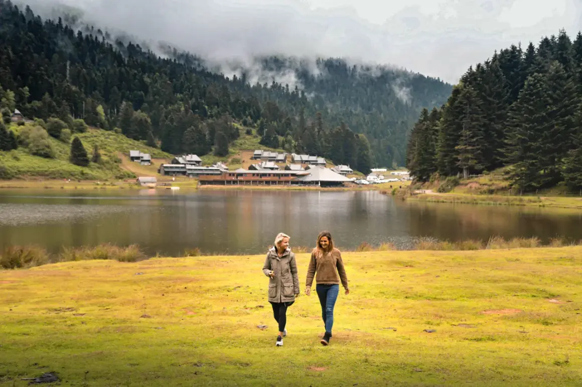 Deux amies profitent d'une promenade au bord du lac de Payolle, entouré de forêts et de montagnes brumeuses.