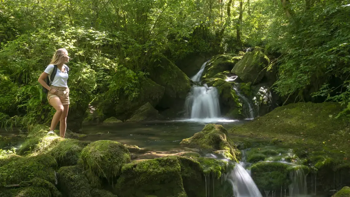 Une randonneuse admire un petit cirque de consolation, une cascade paisible au cœur d'une forêt luxuriante.