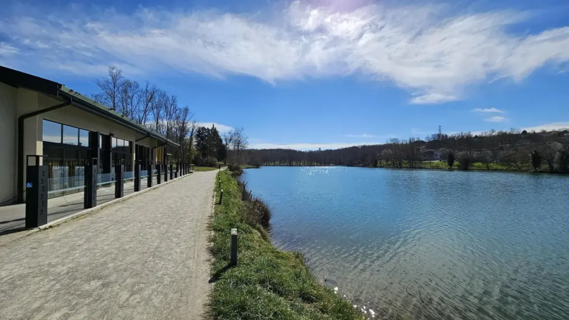 Promenade paisible au bord du lac de Flourens, avec un bâtiment moderne et un ciel bleu éclatant.