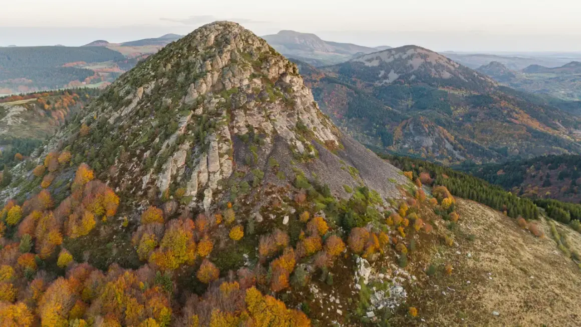 Vue aérienne du Mont Gerbier de Jonc en automne, ses pentes rocheuses et ses forêts aux couleurs flamboyantes. Une carte visuelle de ce paysage volcanique.