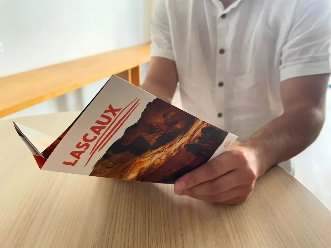 Un homme lit un dépliant sur la grotte de Lascaux, planifiant son itinéraire pour découvrir les peintures préhistoriques.