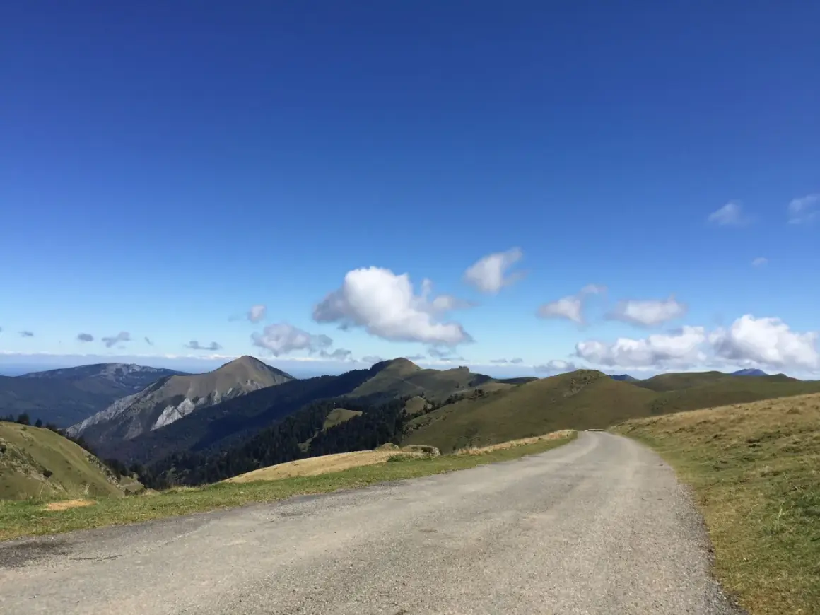 Route sinueuse menant au port de Bales, traversant des paysages de montagnes verdoyantes sous un ciel bleu éclatant.