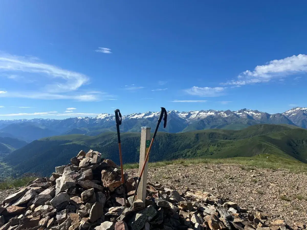Bâtons de randonnée plantés au sommet d'un cairn, offrant une vue panoramique sur les montagnes enneigées et les vallées verdoyantes, un paysage typique du port de Bales.