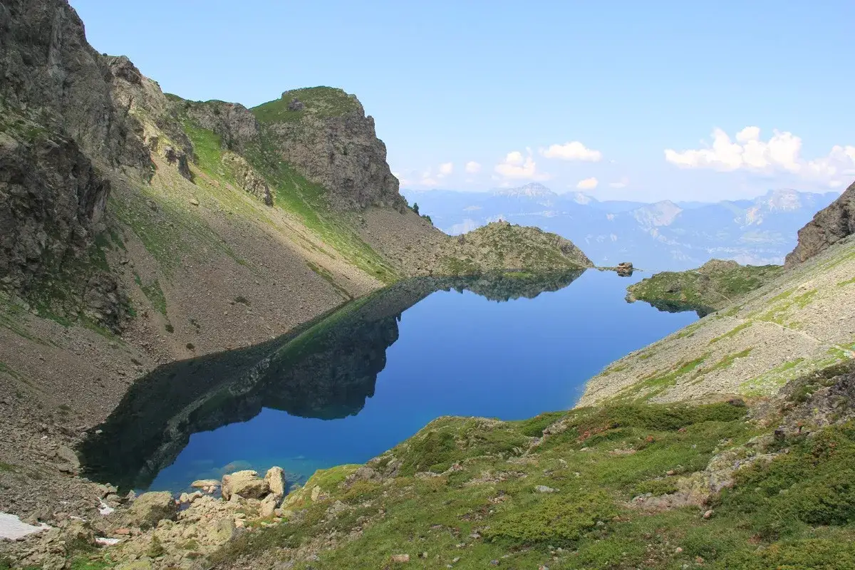 Le lac du Crozet, d'un bleu profond, refl&egrave;te les montagnes escarp&eacute;es et le ciel clair. Un paysage alpin paisible.