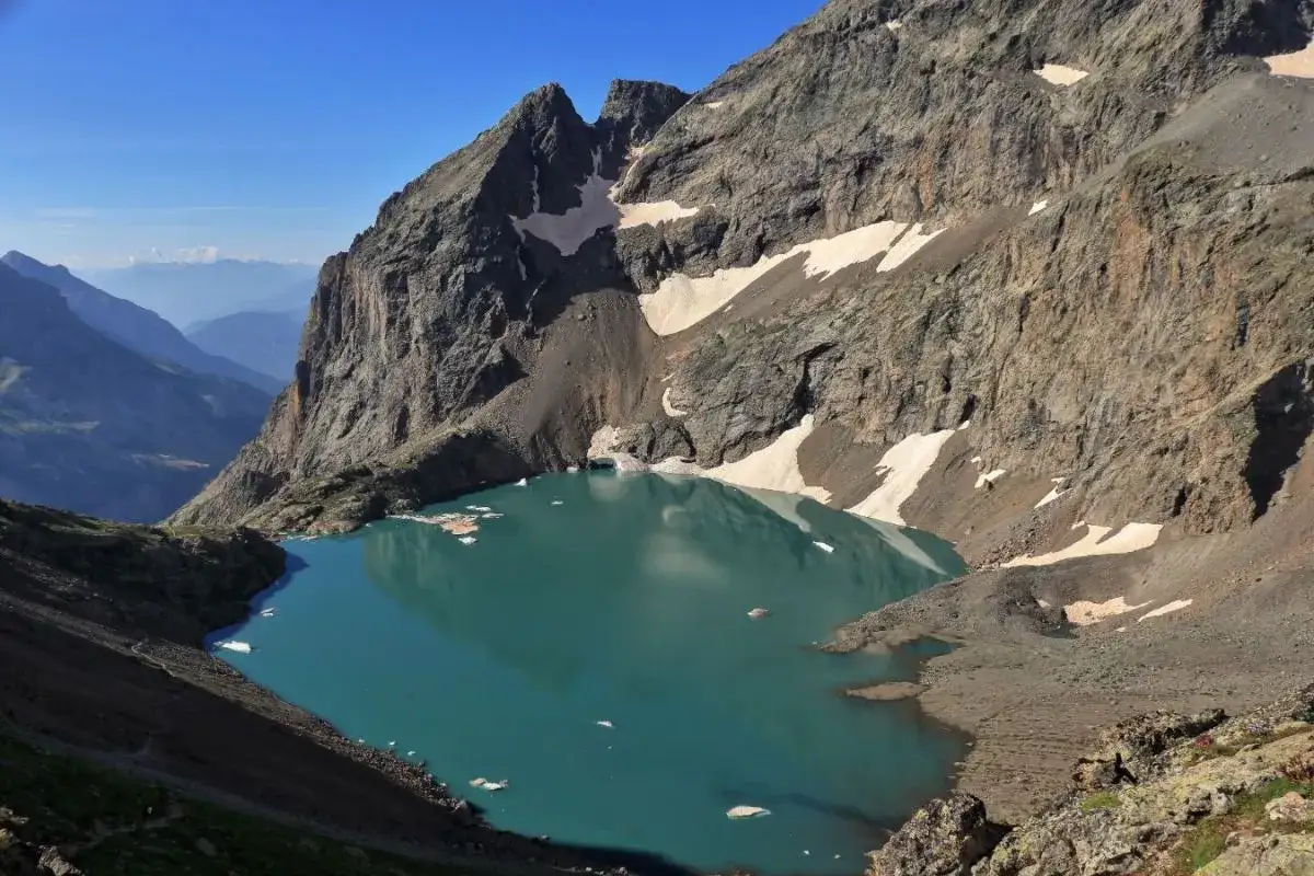 Le lac de l'Eychauda, d'un bleu turquoise saisissant, est niché au creux d'une vallée montagneuse aux pentes abruptes et rocheuses, parsemées de névés.