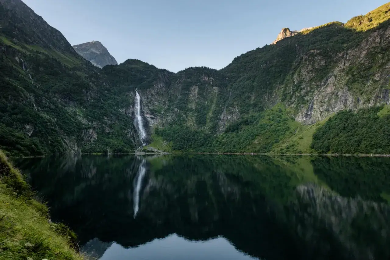 Magnifique cascade se jetant dans le lac de Toulouse, refl&eacute;tant les montagnes verdoyantes sous un ciel clair.