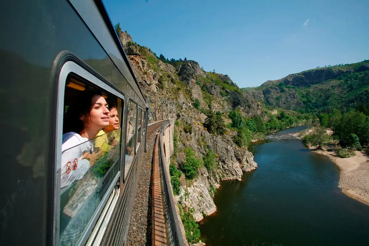 Deux jeunes femmes regardent par la fenêtre d'un train traversant un paysage montagneux. Une idée pour que faire ce dimanche dans le 43.