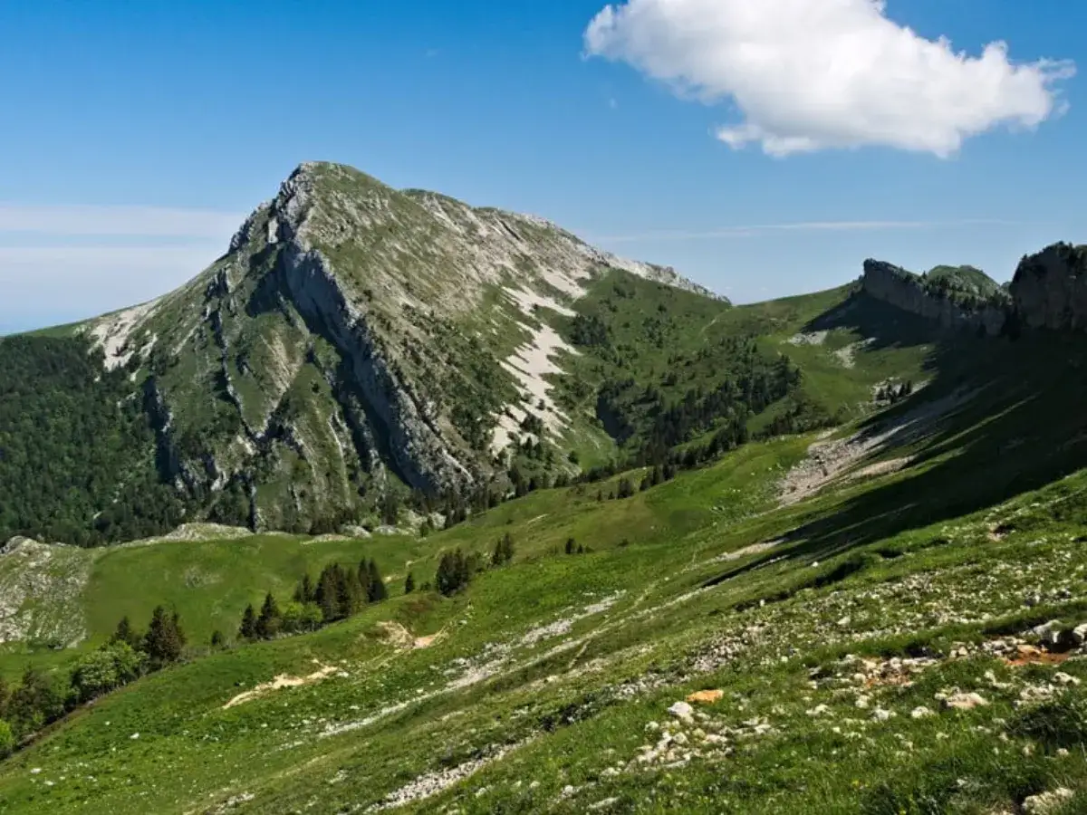 Vue panoramique sur la Grande Sure, un sommet imposant aux pentes verdoyantes et rocheuses, sous un ciel bleu parsemé de nuages.