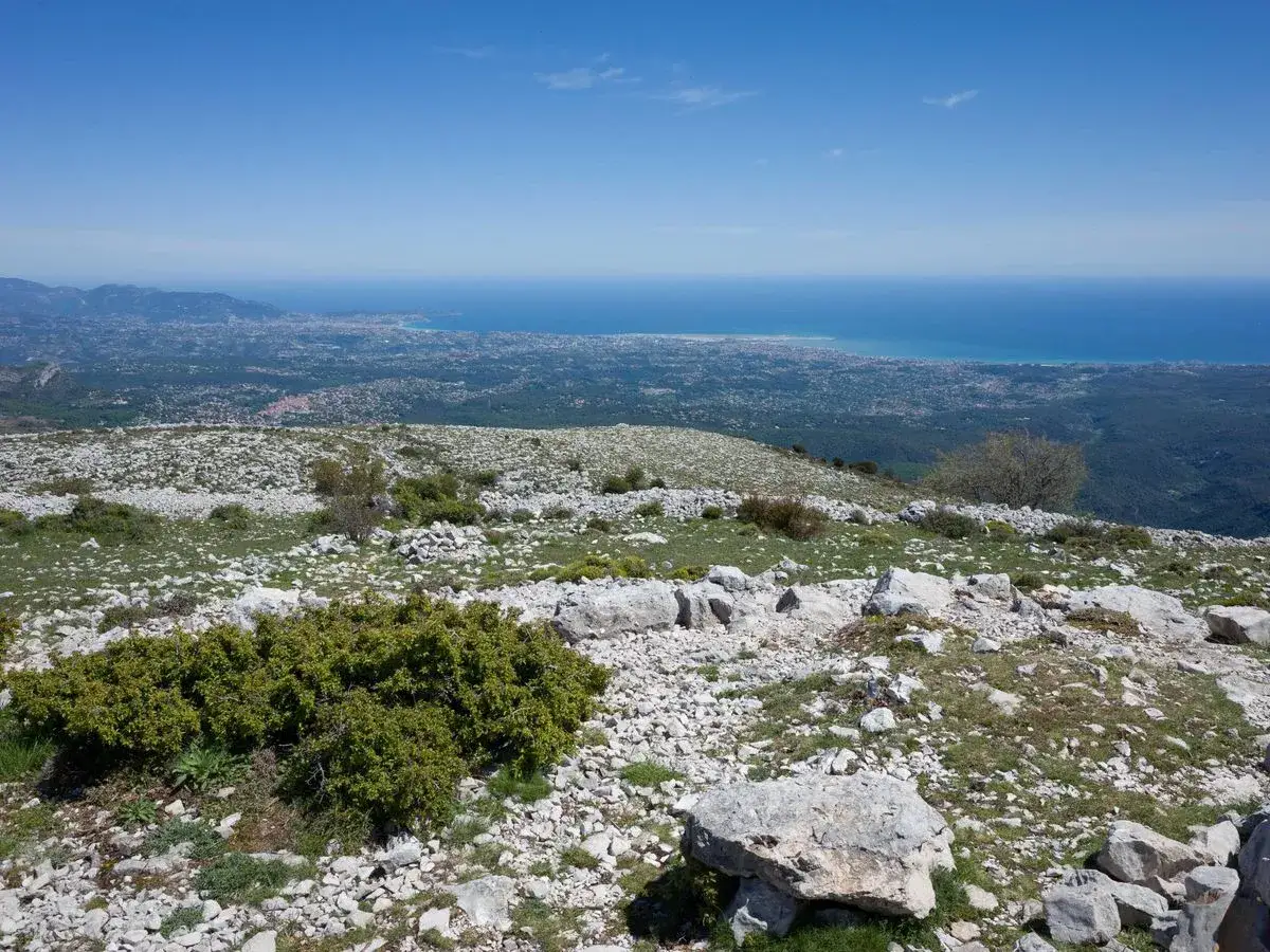 Vue panoramique depuis le pic des Courmettes, avec la mer M&eacute;diterran&eacute;e et la c&ocirc;te au loin. Paysage rocheux et verdoyant.