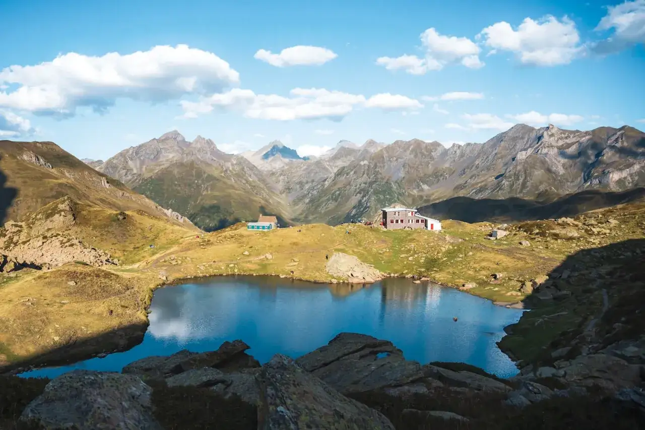 Vue d'un lac de montagne paisible, avec des refuges et des montagnes majestueuses en arri&egrave;re-plan, lors d'un tour du Pic du Midi d'Ossau.