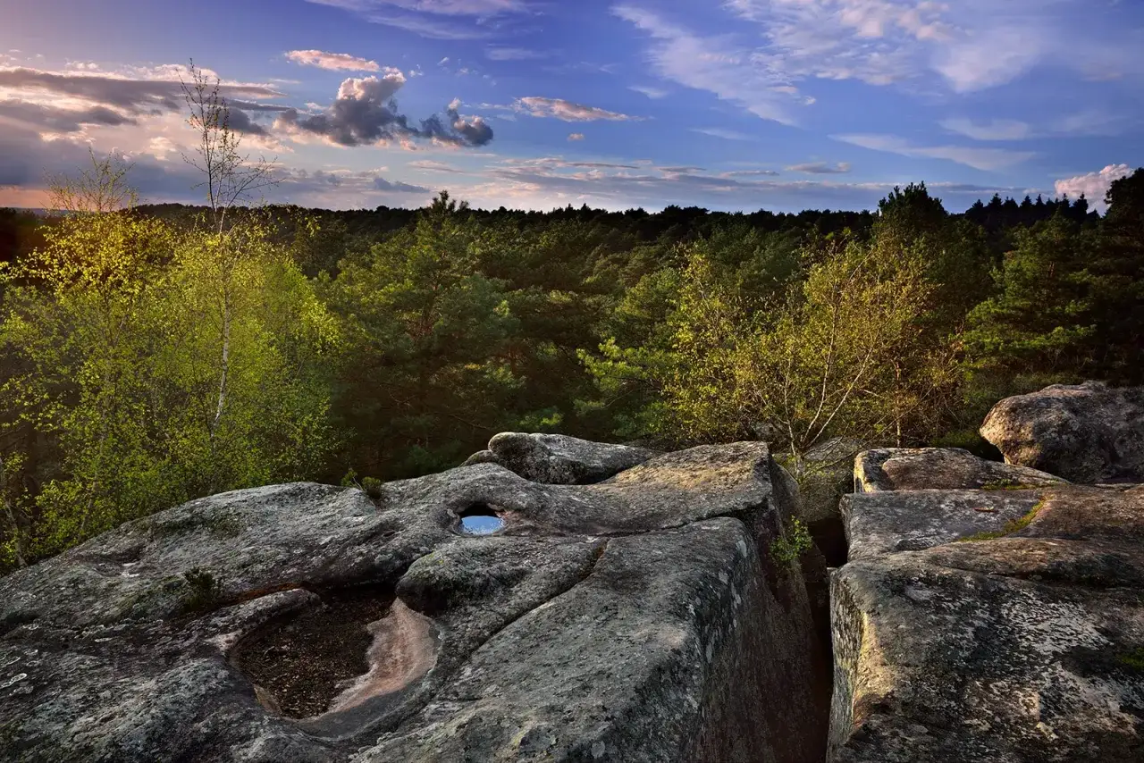 Vue panoramique des gorges de Franchard au coucher du soleil, avec des rochers imposants au premier plan et une for&ecirc;t dense &agrave; perte de vue.