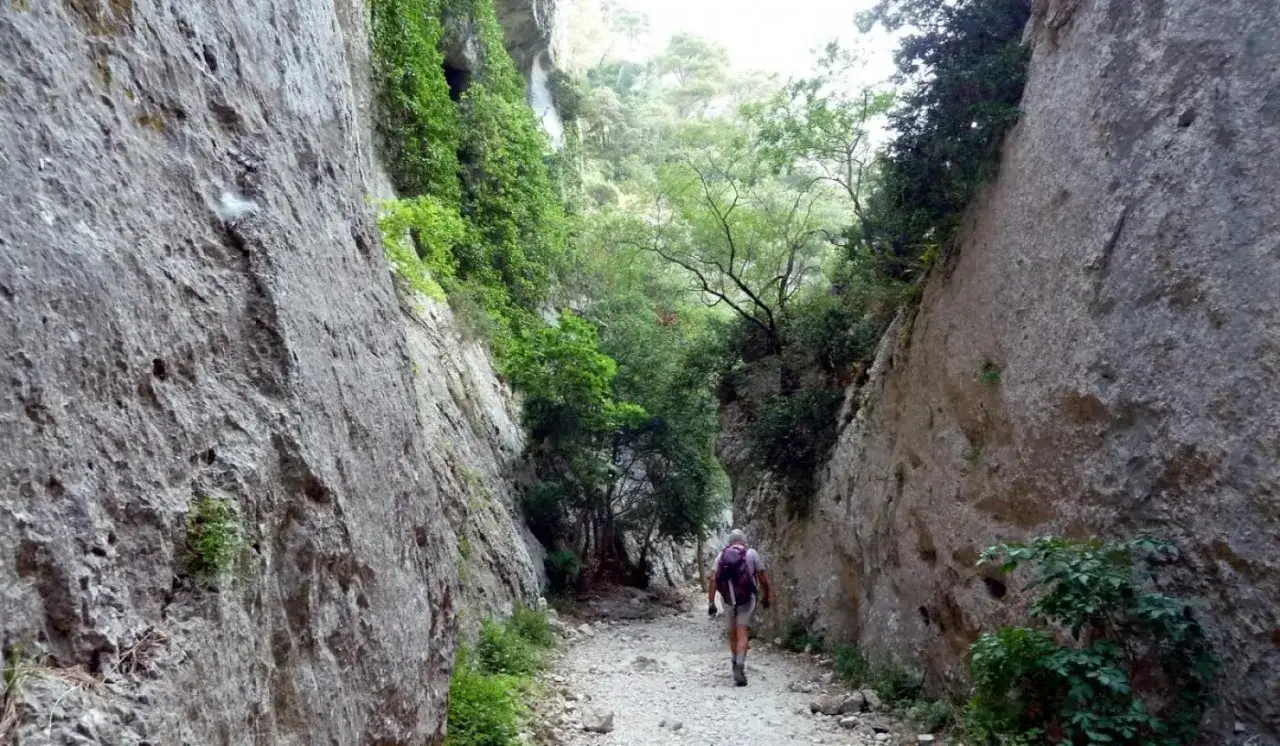 Randonneur dans les gorges du Récalon, un sentier rocailleux serpente entre des falaises abruptes couvertes de végétation. Fermeture du sentier annoncée.