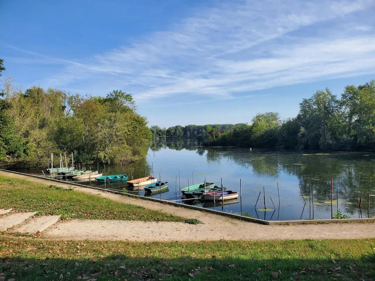 Plusieurs bateaux colorés sont amarrés sur le lac de Viry-Châtillon, sous un ciel bleu parsemé de nuages légers.