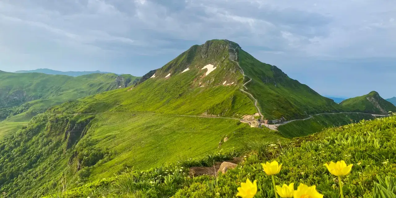 Vue panoramique des montagnes verdoyantes, avec une route sinueuse menant au sommet. Pas de peyrol, juste la beaut&eacute; sauvage de la nature.