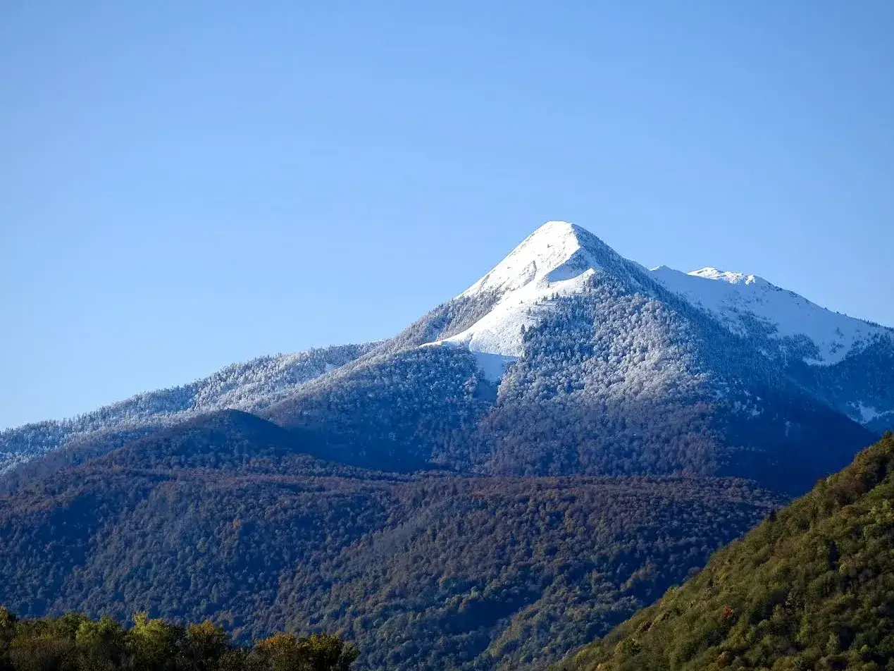 Le pic de Cagire, majestueux et enneig&eacute;, domine un paysage de montagnes foresti&egrave;res sous un ciel bleu clair.