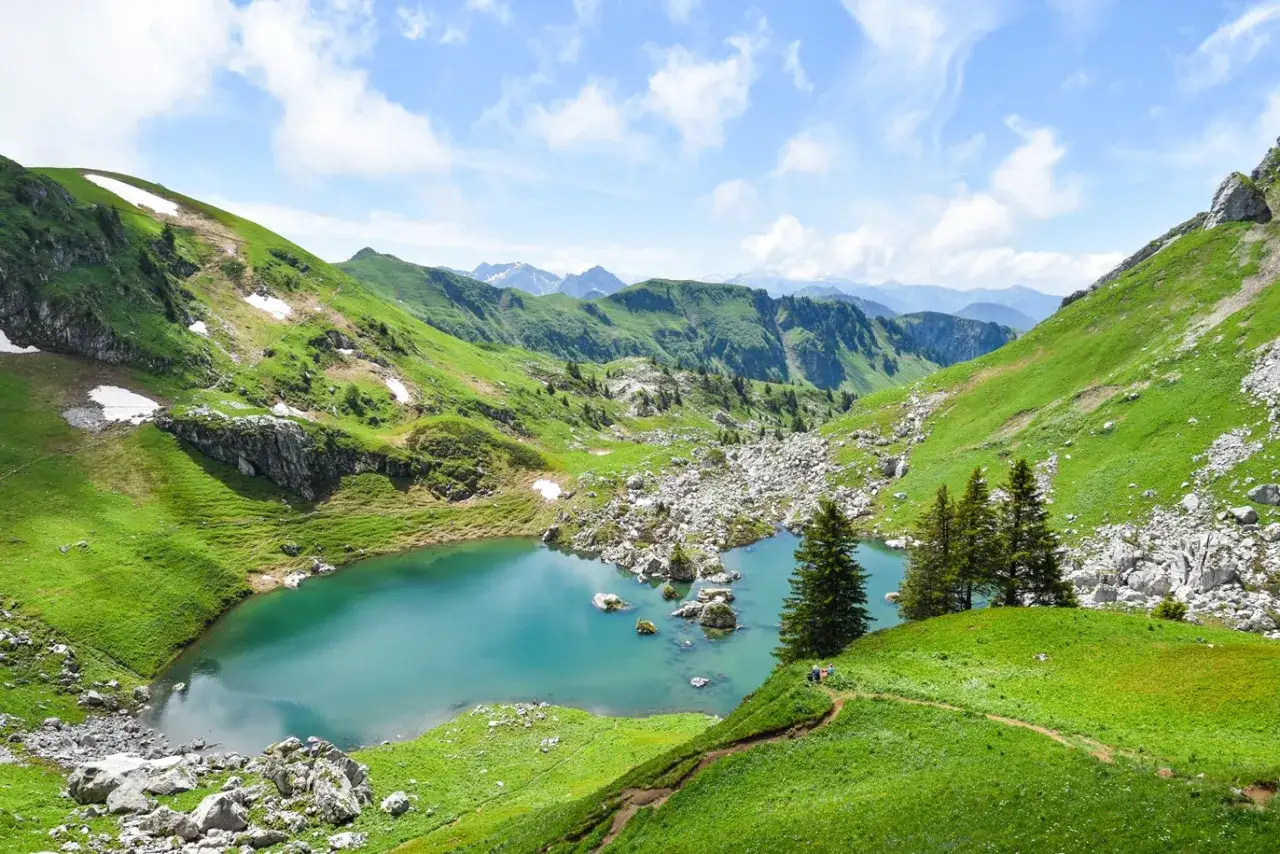 Vue panoramique du lac de Darbon, un joyau turquoise nich&eacute; au c&oelig;ur de montagnes verdoyantes, avec des sentiers serpentant sur les pentes et des sommets enneig&eacute;s &agrave; l'horizon.