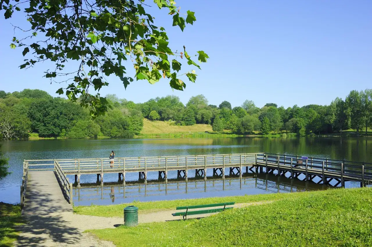 Un ponton en bois traverse le lac Marion &agrave; Biarritz, bord&eacute; d'arbres verdoyants sous un ciel bleu.