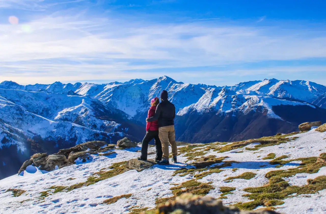 Couple admirant le panorama enneig&eacute; depuis le pic de Gleize. Les montagnes bleues s'&eacute;tendent &agrave; perte de vue sous un ciel clair.