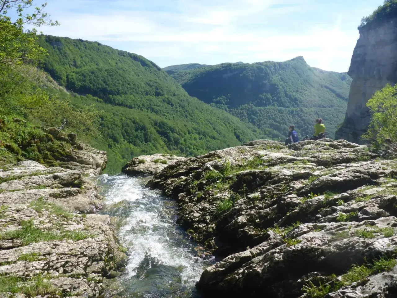 Deux randonneurs contemplent la cascade de la Charabotte, un torrent tumultueux d&eacute;valant une falaise rocheuse au milieu d'une vall&eacute;e verdoyante.