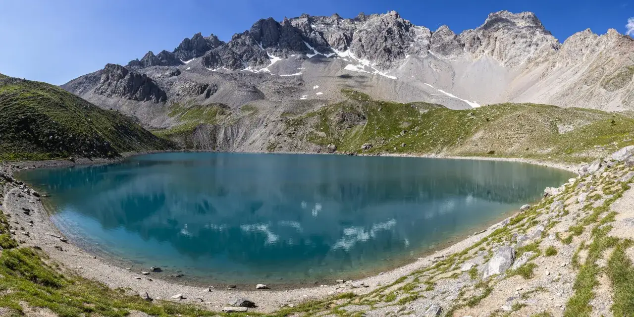 Magnifique lac Saint-Anne aux eaux turquoise, bord&eacute; de montagnes rocheuses et de pentes verdoyantes sous un ciel bleu &eacute;clatant.