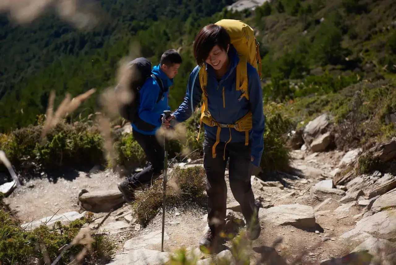 Deux randonneurs escaladent un sentier rocailleux, le soleil illuminant leur chemin vers la cime de Baudon.