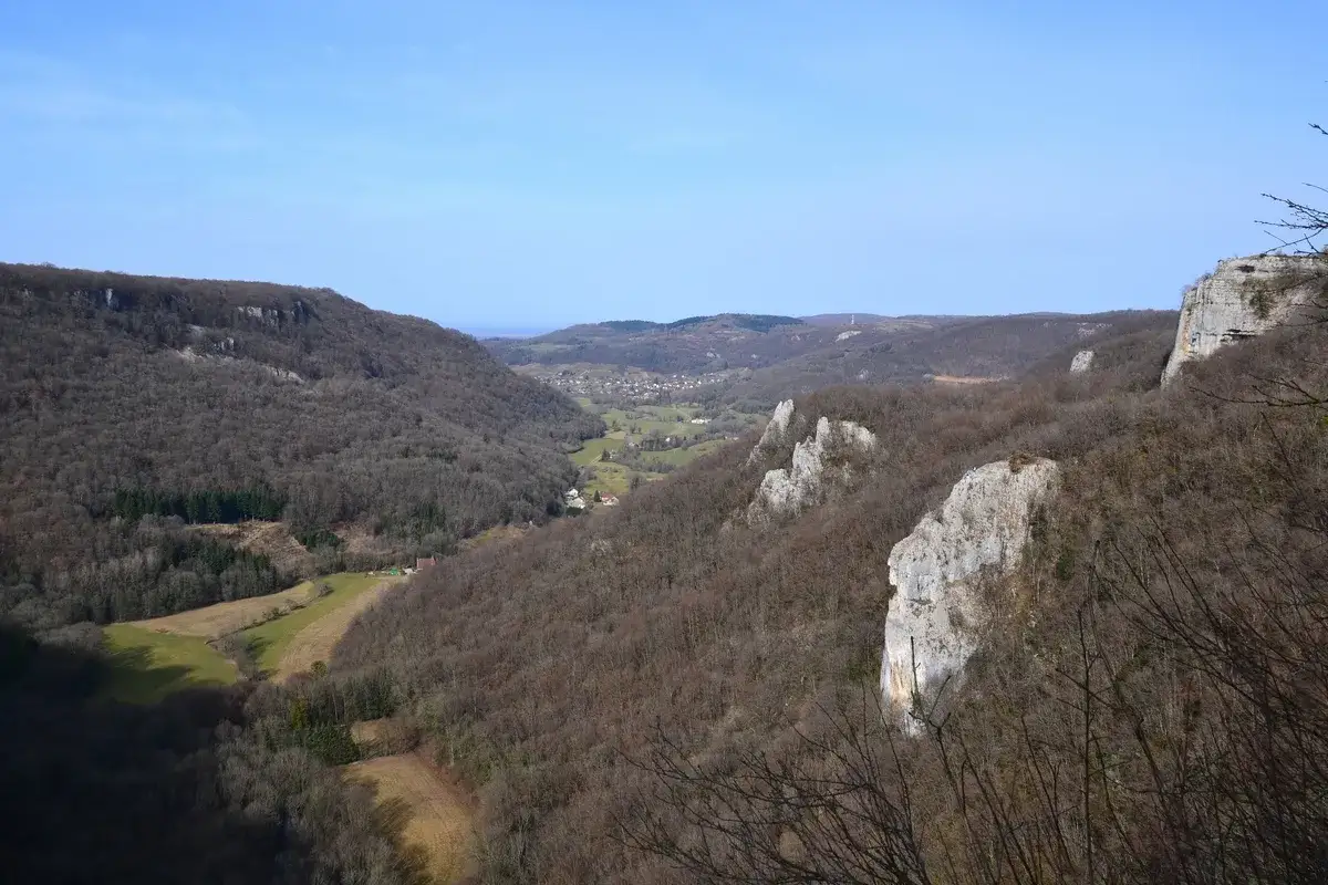 Vue panoramique d'un cirque de consolation boisé, avec des falaises calcaires et un village niché dans la vallée.