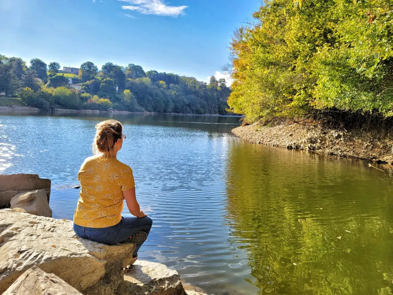 Une femme assise sur des rochers admire le lac, un bel itinéraire dans la forêt de Mervent.