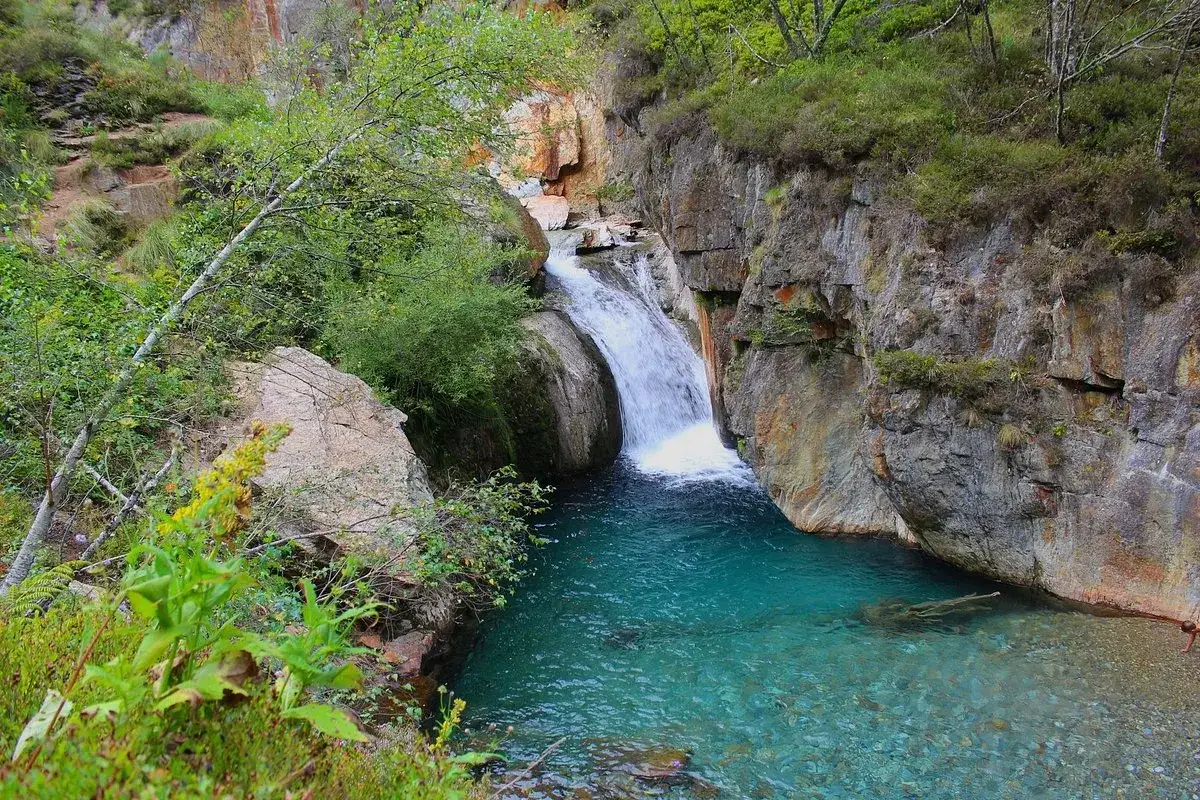 La cascade de l'Artigue d&eacute;vale dans un bassin d'eau turquoise, entour&eacute;e de roches abruptes et de v&eacute;g&eacute;tation luxuriante.