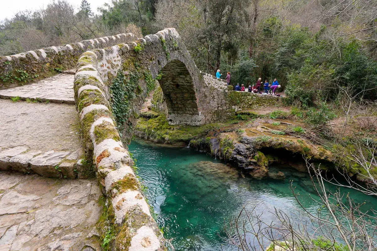 Pont de pierre ancien et verdoyant traversant les gorges de la Siagne aux eaux turquoise. Un groupe de randonneurs admire le paysage.