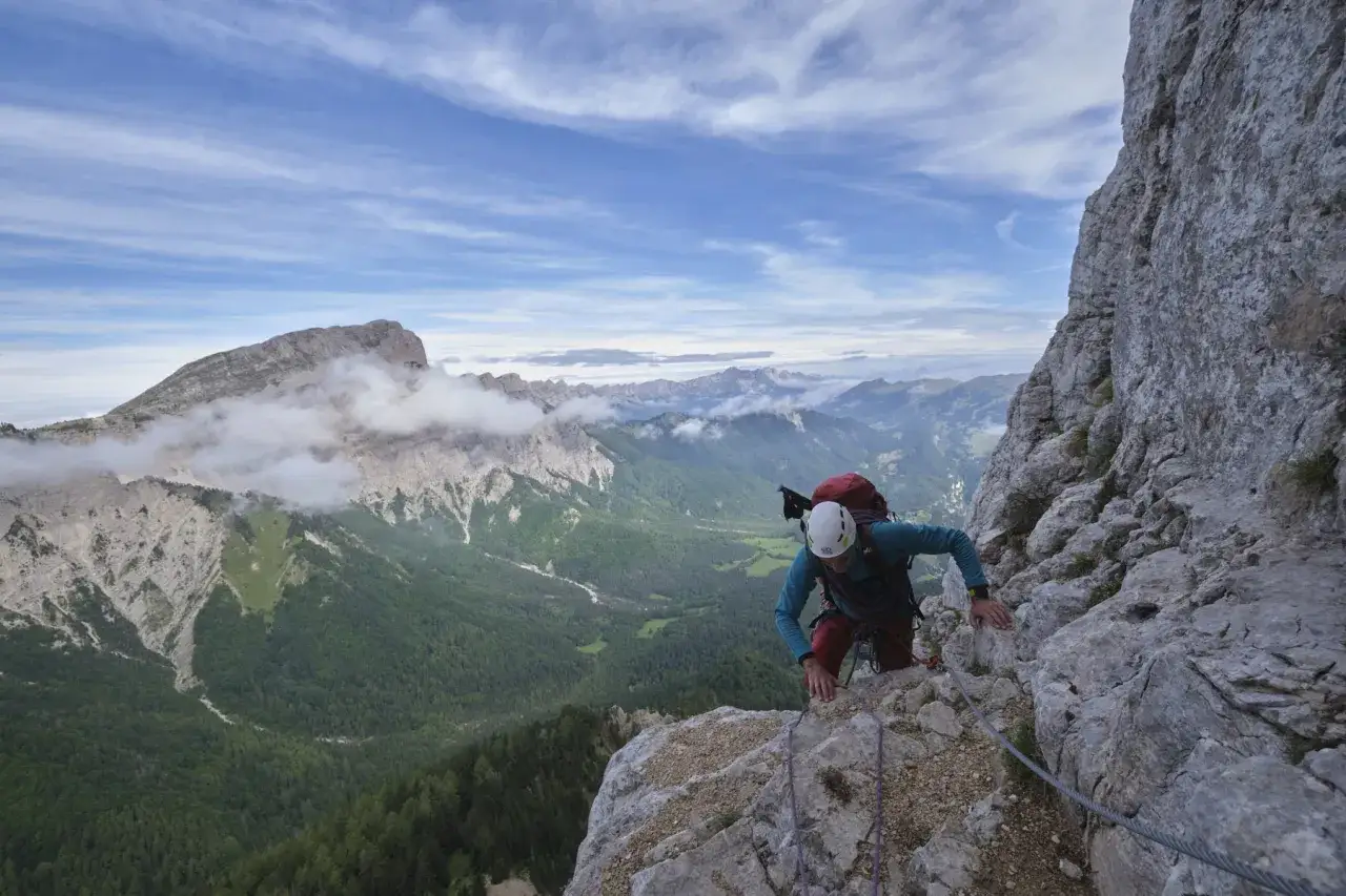 Grimpeur sur un sentier de via ferrata, le pas de l'aiguille. Vue spectaculaire sur les montagnes et la vall&eacute;e verdoyante.