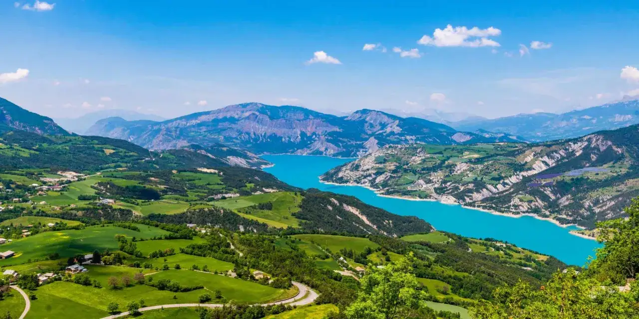 Vue panoramique depuis le pic de Morgon sur un lac turquoise entour&eacute; de montagnes verdoyantes et de champs.