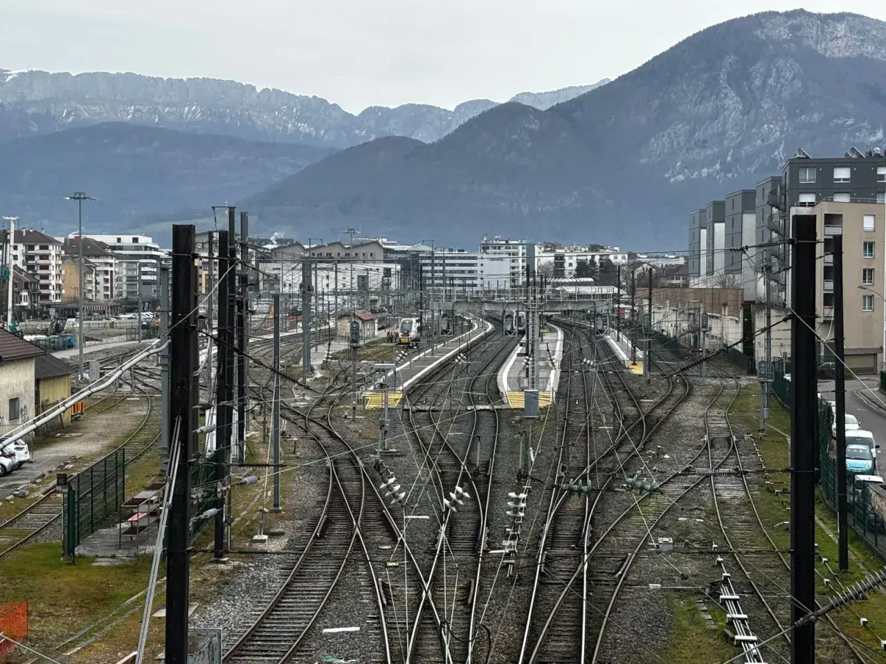 Gare ferroviaire avec de nombreuses voies et caténaires, en arrière-plan des montagnes. Prêt à aller à Annecy.