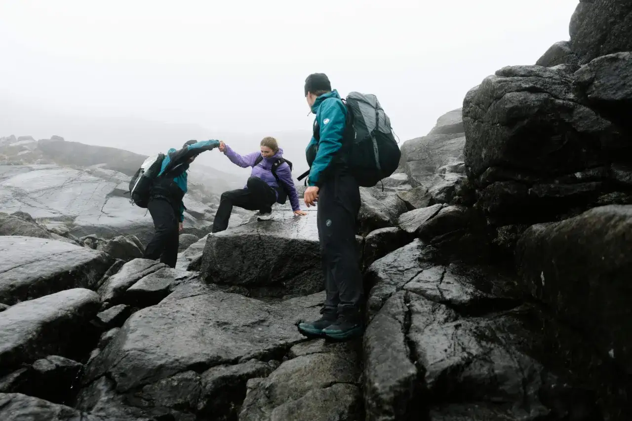 Trois randonneurs s'entraident sur des rochers mouillés par un temps brumeux. Que faire en cas d'orage en montagne ? Ils restent unis.